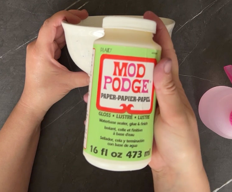 Hand holding Mod Podge over a white bowl