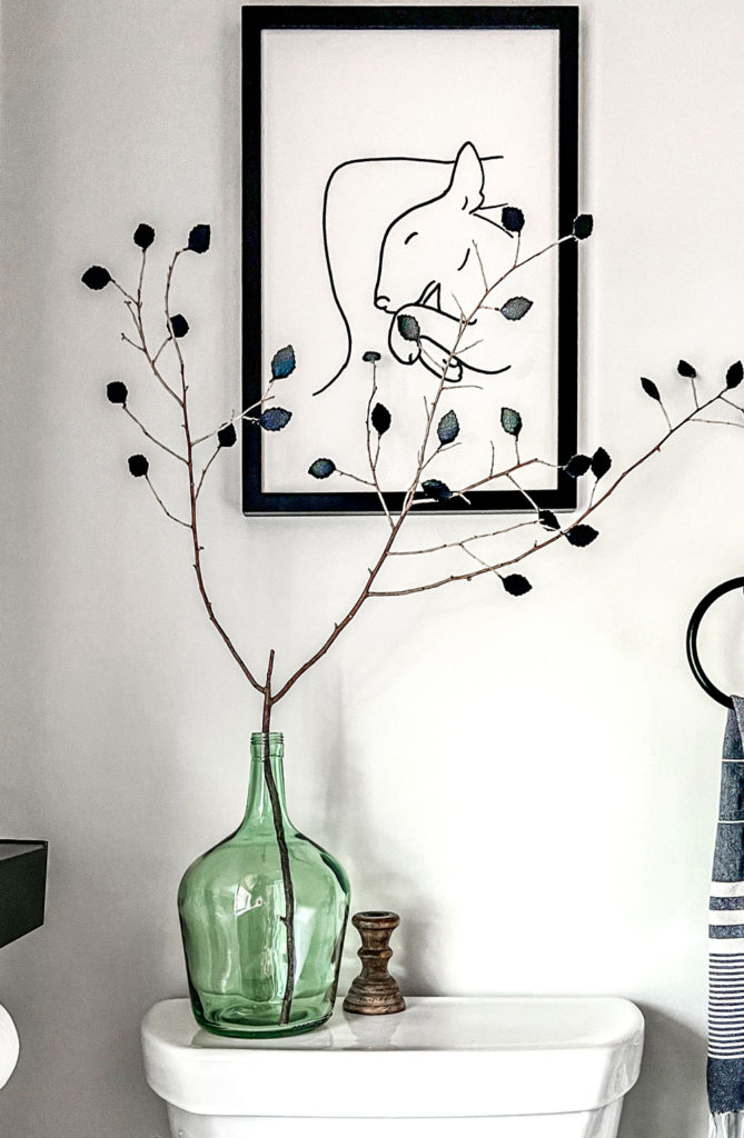 Fake branch with black leather leaves in a green vase against a white wall