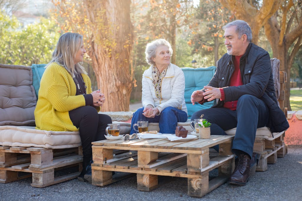 Group of seniors having tea and chatting in a sunny park, enjoying a relaxed moment together.